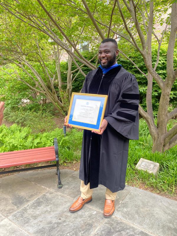 Dr. Meshack Achore in academic regalia holding his framed Lawrence A. Stessin Prize certificate